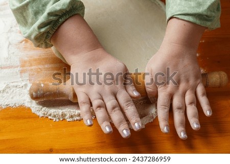 Female hands roll out dough with a rolling pin on a table sprinkled with flour. Horizontal photo