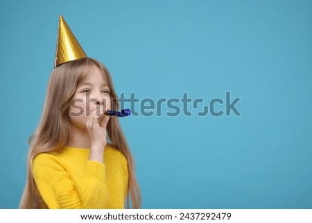 Cute little girl in party hat with blower on light blue background. Space for text