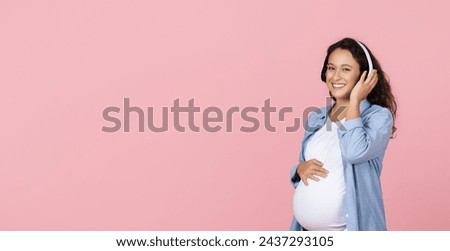 Pregnant woman listening music in headphones on pink background. Young expectant lady enjoying favorite song home, looking at copy space. Relax, leisure, pregnancy concept, web-banner