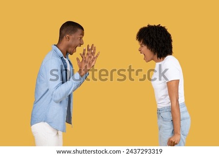 Angry young black man recoils in shock with hands up as a young woman angrily yells at him, both against a stark mustard yellow background. Relationship problems, quarrel, scandal