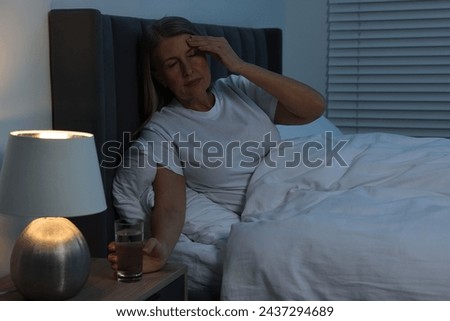Woman with glass of water suffering from headache in bed at night
