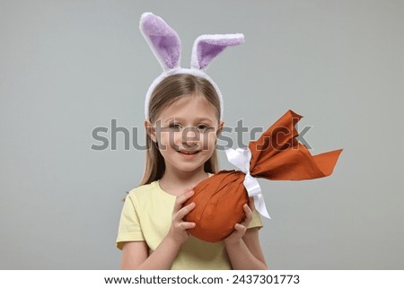 Easter celebration. Cute girl with bunny ears holding wrapped gift on gray background