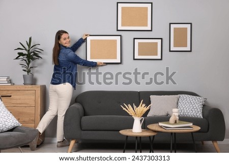 Woman hanging picture frame on gray wall at home