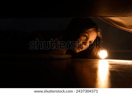 Little girl with flashlight looking for monster under bed at night Royalty-Free Stock Photo #2437304371
