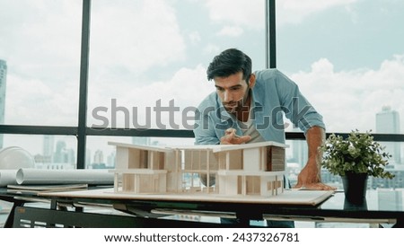Smart caucasian engineer or project manager measure check, inspect, look at house model while standing near panorama window with city, skyscraper view. Manager design house construction. Tracery Royalty-Free Stock Photo #2437326781