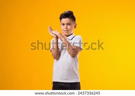 Portrait of smiling kid boy clapping his hands over yellow background Royalty-Free Stock Photo #2437336245