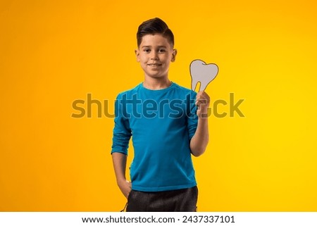 Portrait of child boy holding papercraft tooth over yellow background. Dental health concept