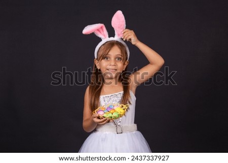 Cute little girl wearing bunny ears on Easter day. Girl holding basket with painted eggs. Royalty-Free Stock Photo #2437337927