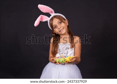 Cute little girl wearing bunny ears on Easter day. Girl holding basket with painted eggs. Royalty-Free Stock Photo #2437337929