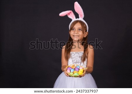 Cute little girl wearing bunny ears on Easter day. Girl holding basket with painted eggs. Royalty-Free Stock Photo #2437337937