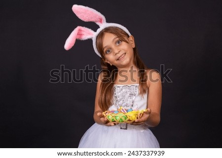 Cute little girl wearing bunny ears on Easter day. Girl holding basket with painted eggs. Royalty-Free Stock Photo #2437337939