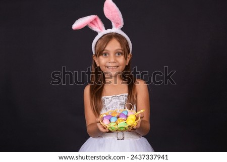 Cute little girl wearing bunny ears on Easter day. Girl holding basket with painted eggs. Royalty-Free Stock Photo #2437337941