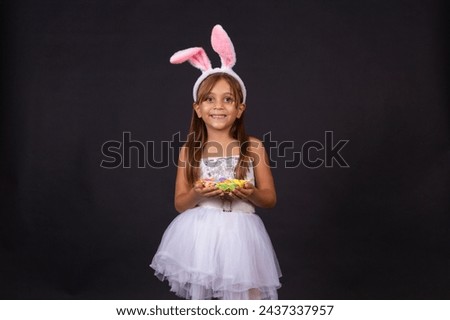 Cute little girl wearing bunny ears on Easter day. Girl holding basket with painted eggs. Royalty-Free Stock Photo #2437337957