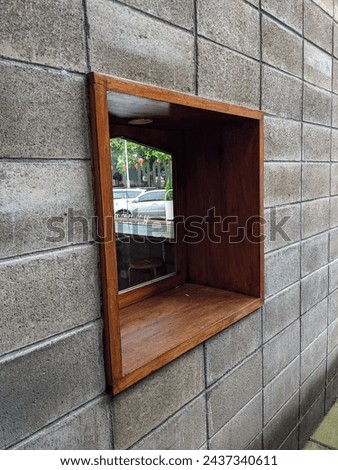 The brown box window is made of wood, attached to the gray wall