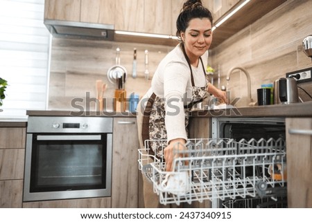 Woman in the kitchen putting dishes in the dishwasher Royalty-Free Stock Photo #2437340915
