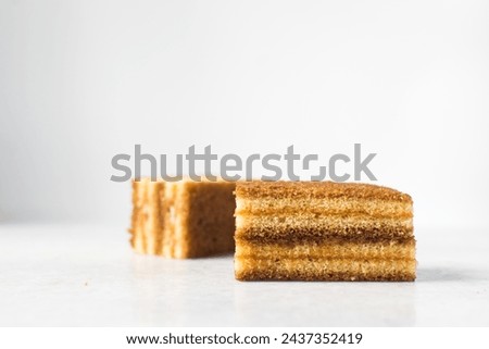 slice of vanilla cake with jam filling, thin layers of vanilla and chocolate cake with jam filling on a white background Royalty-Free Stock Photo #2437352419
