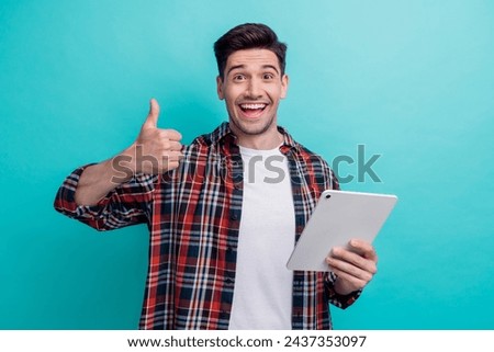 Photo of cute excited man dressed plaid shirt chatting modern gadget showing thumb up isolated turquoise blue color background