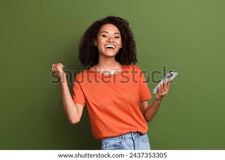 Photo of excited lucky lady dressed orange t-shirt rising fist communicating modern device isolated khaki color background