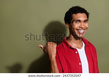 Photo of cheerful cool man dressed red shirt showing thumb back empty space isolated green color background