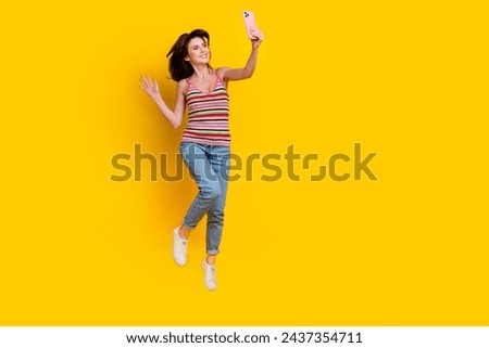 Full size photo of girlish woman dressed knit top jeans jumping making selfie on smartphone isolated on bright yellow color background
