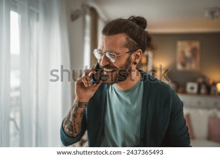 One adult modern man with eyeglasses beard and long hair stand at home use mobile phone talk Royalty-Free Stock Photo #2437365493