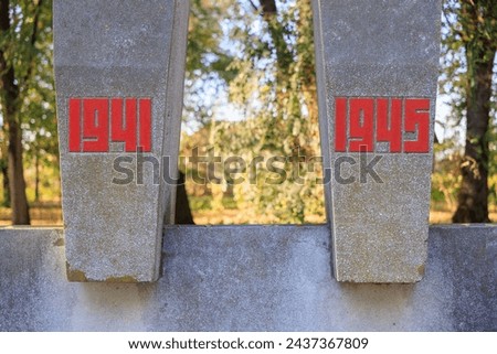 Two concrete pillars with red numbers 1941 and 1945 on them. The pillars are in a park with trees in the background
