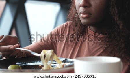 Beautiful African American woman eating pasta with seafood in a restaurant. Woman enjoying food. Close-up