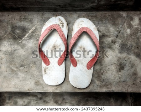 A pair of dull white sandals with red rubber straps that have started to fade in color Royalty-Free Stock Photo #2437395243