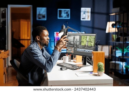 Video editor working on montage clip edit at night, using color grading software on pc at workstation. Young adult videographer working as designer with lights and white balance. Royalty-Free Stock Photo #2437402443