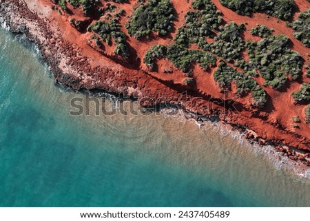 Aerial picture of Cape Peron beach. View from the sky of orange land and  bushes next to the ocean. Location Shark Bay, Western Australia. Top down with a drone. Orange rocks, waves, and blue water.