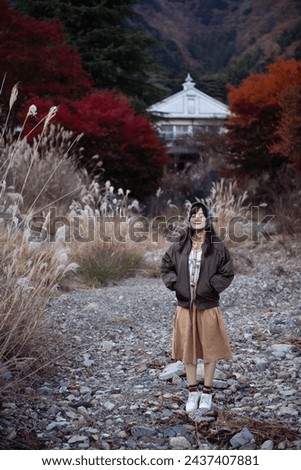 Asian woman in Japan, amidst vibrant fall foliage, smiles in holiday portrait. Friends, selfies, and joyful moments captured by the lake near Mount Fuji.