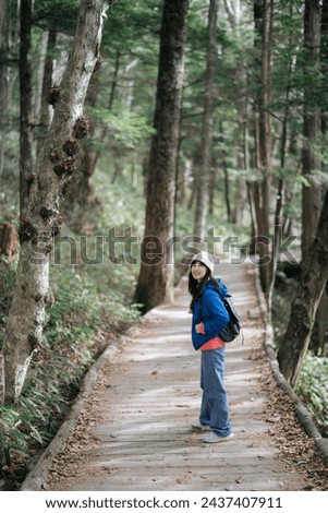 Vibrant fall colors surround an Asian woman in blue jacket on a solo trek. November's joy captured in an elegant portrait by the water in Japan. Royalty-Free Stock Photo #2437407911