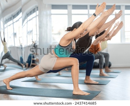 Group of young sporty attractive people practicing yoga lesson with instructor, working out doing version of warrior pose virabhadrasana, indoor full length, studio background Royalty-Free Stock Photo #2437414685