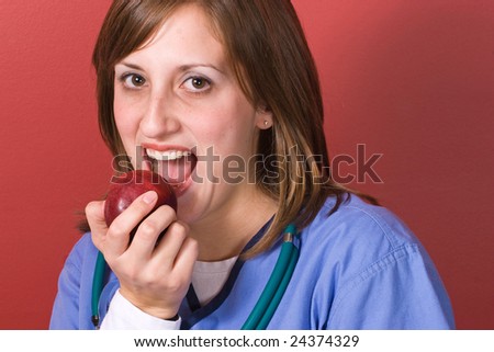 A young nurse bites into a red juicy apple.