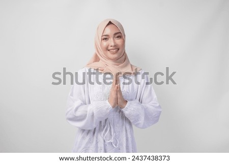Beautiful Asian Muslim woman wearing white dress and hijab smiling while doing formal welcome or greeting gesture, standing over isolated white background Royalty-Free Stock Photo #2437438373