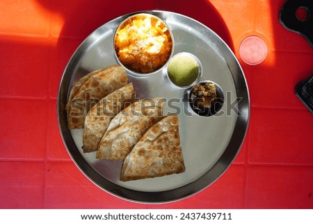 Overhead picture of steel thaali with aloo paratha, Raita, achaar and halwa in it.