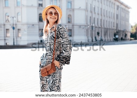 Young beautiful smiling blond hipster woman in trendy summer hippie costume clothes. Carefree female posing in the street at sunny day. Positive model outdoors at sunset. Cheerful and happy in hat
