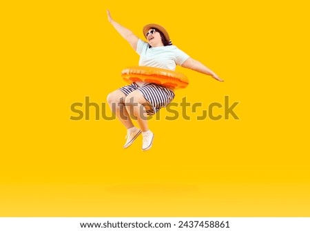 Full body photo of a happy funny fat plus size woman in sunglasses with rubber ring jumping and having fun on studio yellow background. Funny overweight tourist is going on summer holiday trip.
