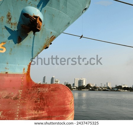 Side wall with anchor on large cargo ship's anchor being pulled. Blue and red ship, While docked at the pier by large ropes on the river, in the background is a view of buildings and transport concept