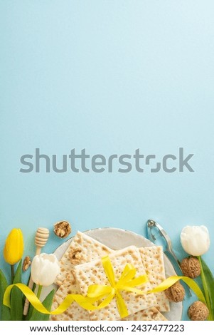 Sophisticated Passover theme: top-view vertical photo showcasing matzah wrapped in ribbon, nuts, egg, honey dipper, nutcracker, and tulips on a gentle blue background, space for message