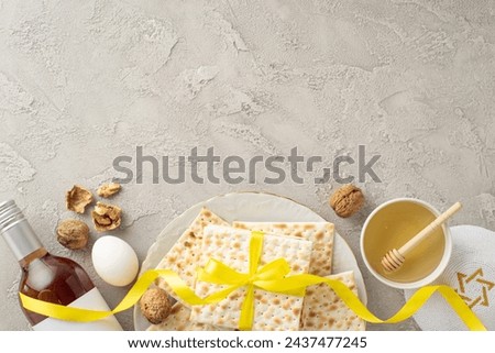 Modern Pesach display concept: top view of a plate with matzah in a yellow ribbon, red wine bottle, walnuts, egg, honey dip, and kippah, arranged on a textured concrete surface, space for copy Royalty-Free Stock Photo #2437477245