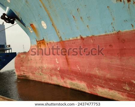 Side wall with Anchor on large cargo ship's anchor being pulled. Blue and red ship, While docked at the pier by large ropes on the river, in the background is a view of the city and transport concept