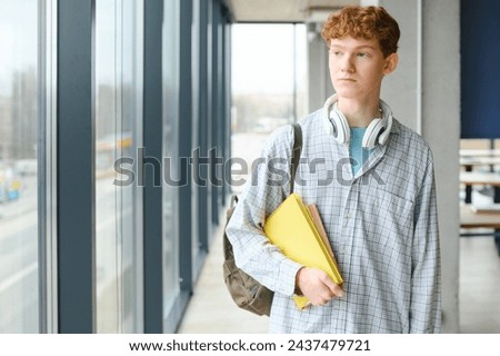 Portrait of smiling smart curly haired teenage boy holding book looking at camera. Back to school, Education concept.