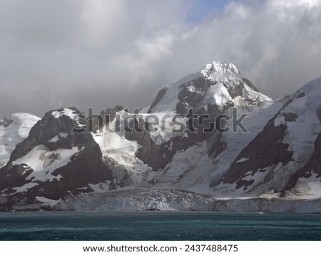    approaching the formidable mountain peaks, icebergs,  and glaciers of elephant island,  on the antarctic peninsula, on a  summer cruise on a  stormy day         Royalty-Free Stock Photo #2437488475