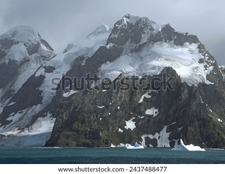    approaching the formidable mountain peaks, icebergs,  and glaciers of elephant island,  on the antarctic peninsula, on a  summer cruise on a  stormy day         Royalty-Free Stock Photo #2437488477