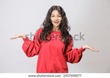 Surprised and Shocked Pakistani girl showing product. Beautiful Pakistani girl with curly hair pointing to side .Presenting your product. Isolated on white background. Expressive facial expressions Royalty-Free Stock Photo #2437490077