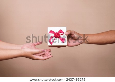 Man's hand giving a gift box with red ribbon to woman 