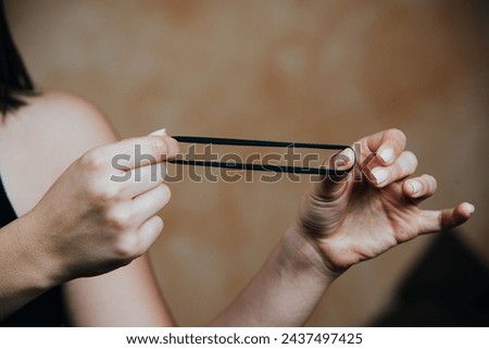 A person's hands manipulating a black hair elastic, a common hair accessory used for styling Royalty-Free Stock Photo #2437497425