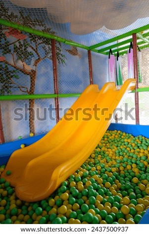 Yellow slide at indoor playground against colourful plastic balls. Yellow sliding board for kids. Empty colorful slides fun activity holiday entertainment.