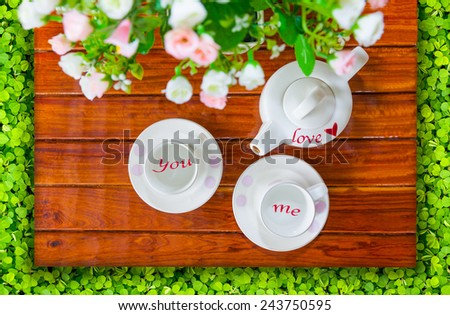 Top view of the teapot, empty teacup or coffee cup and artificial flowers on a wooden and green clover, Love of you and me concept